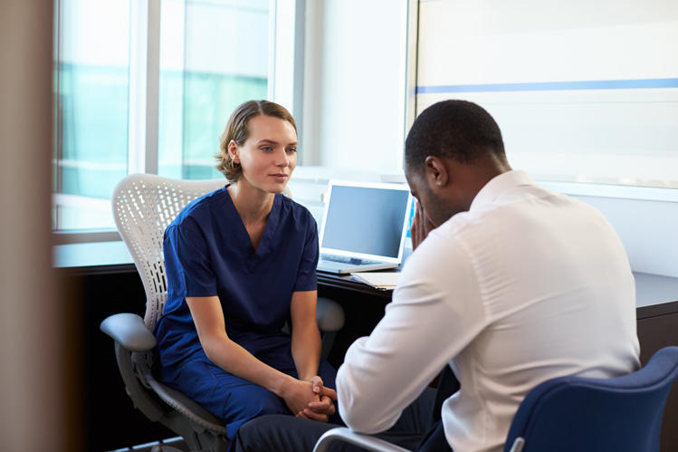 Mental health therapy in New Jersey is provided by a clinician in blue scrubs listening to a man during a consultation in a bright office.
