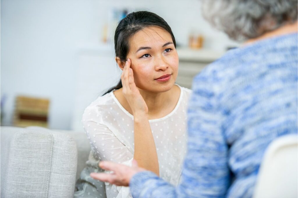 Childhood trauma treatment helps this distressed young woman sitting against a brick wall with her knees pulled to her chest, looking overwhelmed.