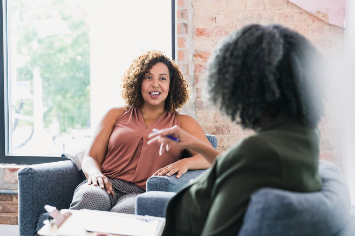 Diverse women smile and interact in a supportive dialectical behavioral therapy group counseling session at a modern New Jersey clinic.