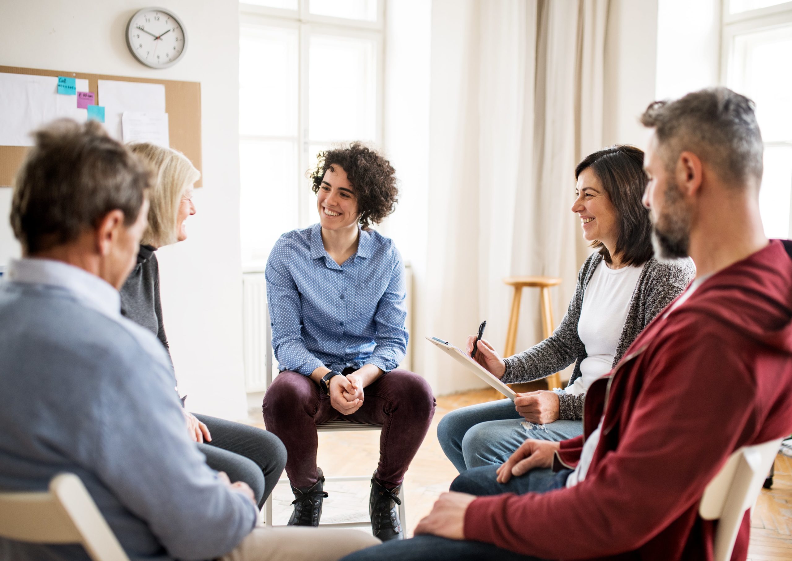 group therapy in New Jersey sessions feature a diverse group sitting in a circle of chairs, sharing smiles in a bright, sunlit community room.