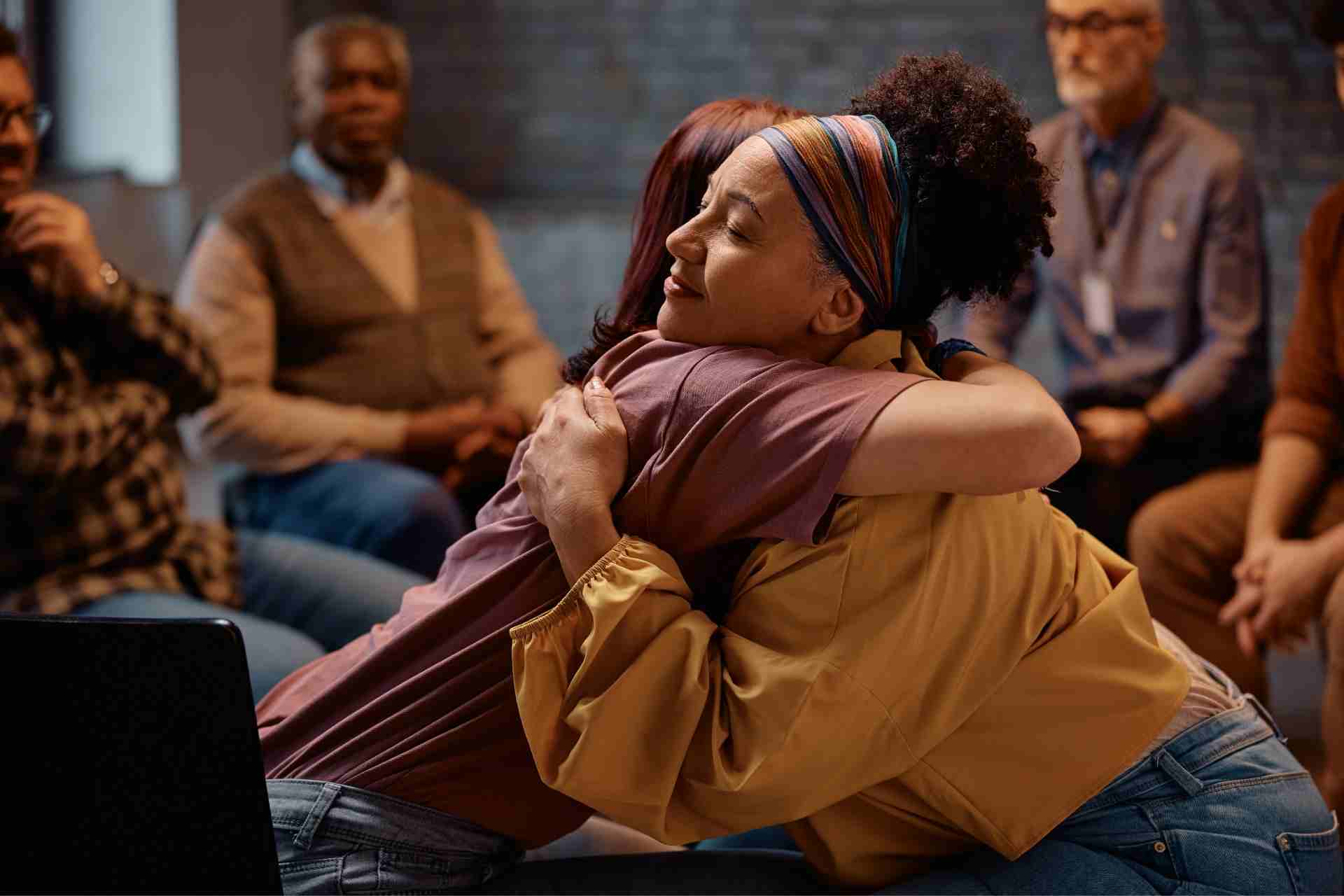 Two participants embrace during a mental health support group session after making progress in PHP and IOP treatment.